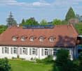 Two-story house with red-tiled roof, multiple dormer windows, white siding, and a well-maintained garden.