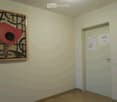 Empty room with light-colored walls, wooden floor, and a single door. A framed abstract painting is mounted on one wall.