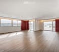 Empty room with wooden flooring, large windows, and sliding glass doors leading to a balcony.