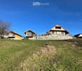 Residential houses with pitched roofs and balconies, surrounded by a grassy slope and stone wall.