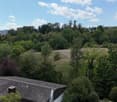 A panoramic view of a suburban area with houses, trees, and a field, under a partly cloudy sky.