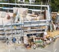 A multi-story building under construction with scaffolding, exposed steel beams, and construction materials scattered around the site.