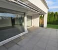 Modern glass sliding door opens to a tiled balcony area with a view of the garden and surrounding trees.