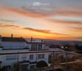 Balcony overlooking a scenic sunset view of a residential area with houses, solar panels, and distant hills.