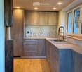 Modern kitchen with wooden ceiling, light wood flooring, stainless steel sink, and grey cabinets.