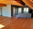 Modern kitchen with wooden flooring, grey cabinets, and a kitchen island. Features a sink, faucet, and a coffee machine.