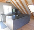 Modern kitchen with grey cabinets, a central island, and a black countertop, featuring wooden beams and skylights.