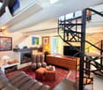 Cozy living room with exposed wooden beams, fireplace, leather sofa, armchairs, coffee table, TV, and artwork on the walls.
