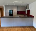 Modern kitchen with grey cabinets, a dark countertop, a sink with a faucet, and an oven in the background.
