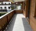 Balcony with wooden railings, tiled floor, and a view of the surrounding buildings and greenery.