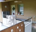 Balcony with wooden railing, bench, towel, vase on window sill, and a small storage area with boxes.