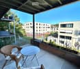 Balcony with a round table, two wicker chairs, and a view of modern buildings and greenery.