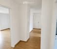 Empty hallway with light wooden flooring and white walls, featuring a closed door at the end and a mirror on the left wall.