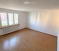 Empty room with wooden flooring, white walls, and a window with a radiator below it.