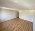 Empty room with light wooden flooring and white walls, featuring an open doorway leading to another space.