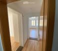 Empty hallway with wooden flooring, white walls, and open doors leading to other rooms.