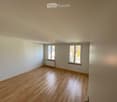 Empty room with wooden flooring, white walls, and two windows with metal frames. A radiator is visible under one window.