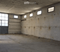 Empty industrial-style room with concrete walls and floor, large windows, and a metal door.