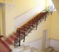 Elegant staircase with ornate wrought iron railing, red patterned carpet, and light yellow walls.