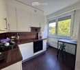 Modern kitchen with white cabinets, dark wooden countertops, and stainless steel appliances. Features a sink, oven, and a small dining area with a table and stool.