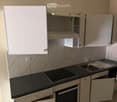 Modern kitchen with white cabinets, black countertops, a sink, and an oven. The backsplash features a geometric tile pattern.