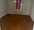 Empty room with wooden flooring, white walls, and a window with pink shutters.