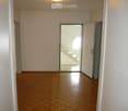 Empty hallway with wooden flooring, white walls, and a glass door leading to a balcony area.