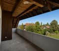 Balcony with wooden roof, concrete floor, and a view of a green landscape with trees and houses.