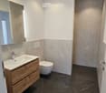 Modern bathroom with dark marble tiles, a wooden sink cabinet, a toilet, and a large mirror.