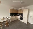 Modern kitchen with light wood cabinets, stainless steel appliances, and a small dining area with a table and chairs. A cat is resting on the floor near the door.