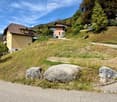 Residential area with multi-story houses, a raised ground floor, and a grassy slope with large rocks.