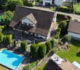 Aerial view of a two-story house with a well-maintained garden, a swimming pool, and surrounding greenery.