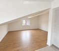 Empty room with wooden flooring and white walls, featuring a window with a view of a house and a tree outside.