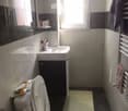 Modern bathroom with a sink, mirror, toilet, and shower. The walls are tiled in a combination of dark and light colors, and there is a towel hanging on the side.