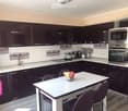 Modern kitchen with dark cabinets, white countertops, and stainless steel appliances. Features a sink, microwave, oven, toaster, and a small dining area with a table and chairs.