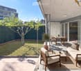 Modern outdoor patio with a sofa, chairs, coffee table, dining table, and potted plants, overlooking a well-maintained garden.