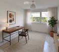Modern, well-lit room with a wooden desk, chair, table lamp, picture frame, potted plant, and decorative vases.