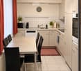 Modern kitchen with white cabinets, a dining table with four chairs, microwave, coffee maker, sink, and various appliances.