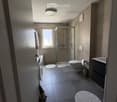 Modern bathroom with a glass-enclosed shower, toilet, sink, and a large window providing natural light. Features include a round rug, a towel hanging on the wall, and a trash can near the toilet.