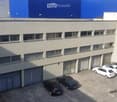 A multi-story building with a flat roof, multiple windows, and several garage doors. Several cars are parked in front of the building.