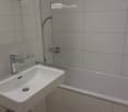 Modern bathroom with a white sink, chrome faucet, bathtub, and showerhead. Light gray tiles on walls and a beige tiled floor.