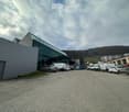 Modern industrial building with a glass facade and a parking lot with several vehicles, including vans and cars.