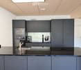 Modern kitchen with dark grey cabinets, stainless steel appliances, and a sleek black countertop.