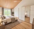 Modern bedroom with a large bed, nightstand, lamp, mirror, wardrobe, and potted plants. The room features wooden flooring, large windows with a scenic view, and a cozy atmosphere.