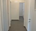 Empty hallway with white walls, grey tiled floor, and several doors leading to other rooms.