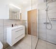 Modern bathroom with a white sink cabinet, mirror, glass-enclosed shower, and a bottle on the sink.