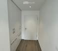 Empty hallway with white walls, wooden flooring, and a white door at the end.