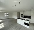Modern kitchen with white cabinets, black countertops, and a central island. Features a sink, oven, microwave, and ample natural light from large windows.