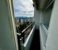 Balcony with metal railing, overlooking a cityscape with buildings, trees, and parked cars.