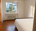 Bright bedroom with wooden parquet flooring, a single bed with white bedding, a radiator below a large window, and modern ceiling lights.